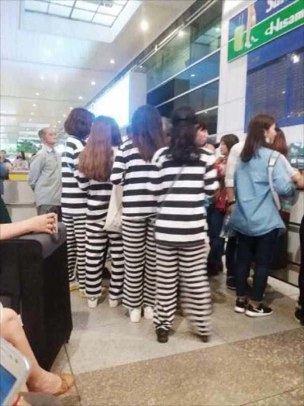 Các bạn trẻ mặc đồ phạm nhân đợi check-in tại cửa sân bay.