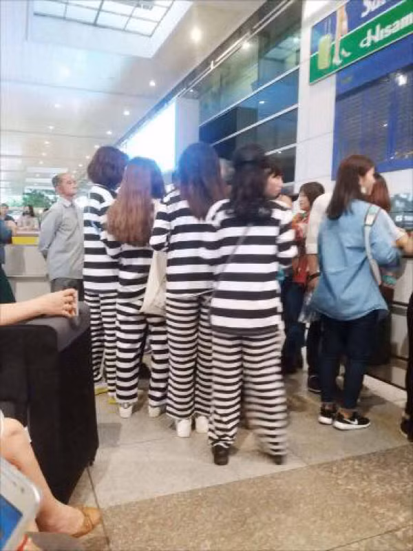 Các bạn trẻ mặc đồ phạm nhân đợi check-in tại cửa sân bay.