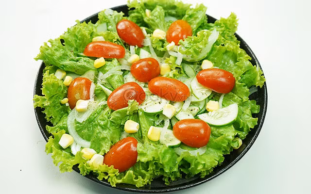 Trộn tỏi ớt với dầu olive, dấm nho, đường, nước mắm trong 1 chén nhỏ. Tưới chén gia vị lên tô xà lách rồi trộn đều bằng tay và hơi bóp nhẹ để rau ngấm gia vị. Rắc ngô và dưa chuột thái lát lên đĩa xà lách là hoàn thành. Ảnh: Cooky.vn.