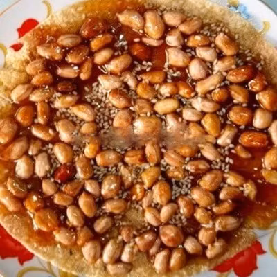 Kẹo cu đơ từ lạc. Nguyên liệu: Bánh đa vừng loại mỏng, lạc, mật mía, nước cốt gừng, gừng sợi, mẻ rang, bột mạch nha. Lạc rang giòn, bỏ vỏ. Bánh đa cắt thành miếng tròn. Bắc chảo cho mật mía vào đun cho tan chảy, cho thêm nước cốt gừng và bột mạch nha vào đảo đều tới khi mật mía đông đặc. Ảnh: cooky.vn.