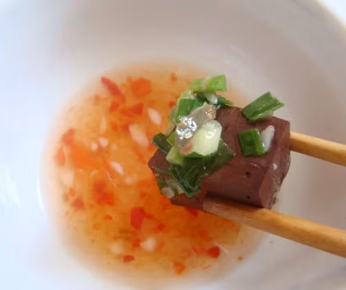 Làm nước mắm: Dầm ớt, tỏi cho nhuyễn, cho chanh, đường, nước lọc khuấy đều tay cho đường tan, cuối cùng cho nước mắm vào, nêm nếm cho vừa ăn. Cho tiết vào bát, rưới mỡ hành lên trên, cho nước mắm vào ăn chung. Ảnh: bepgiadinh.com.