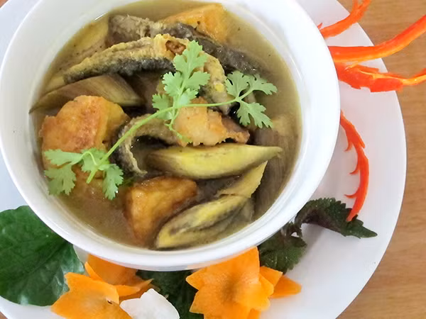 Phi thơm hành, cho thịt ba chỉ thái miếng vừa ăn, đậu phụ đã rán vào, cho chuối xanh vào xào cho ngấm gia vị. Trút hỗn hợp chuối xanh xào ba chỉ vào nồi chạch đang om, thêm ít nước sôi, nêm nếm vừa ăn, om nhỏ lửa 20 phút. Cho hành hoa, tía tô, mùi tầu, lá lốt rồi tắt bếp. Ảnh: thitruongthuoc.com.