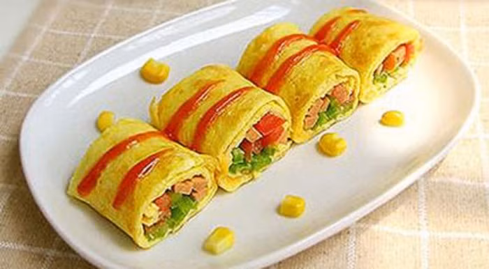 Rau cuộn trứng chiên. Nguyên liệu gồm trứng gà, bông cải xanh, nấm rơm, cà chua, cà rốt, sữa tươi, nước mắm. Tất cả các loại rau củ hấp chín và băm thô. Trứng gà đánh tan với nước mắm, thêm thìa sữa tươi vào. Sau đó, bắc chảo dầu và cho trứng vào dát thật mỏng. Khi thấy trứng còn ướt mặt, rắc rau củ đã băm và cuộn lại. Tiếp tục rán thêm một chút để rau củ bám chặt vào trứng. Ảnh: Phununews.