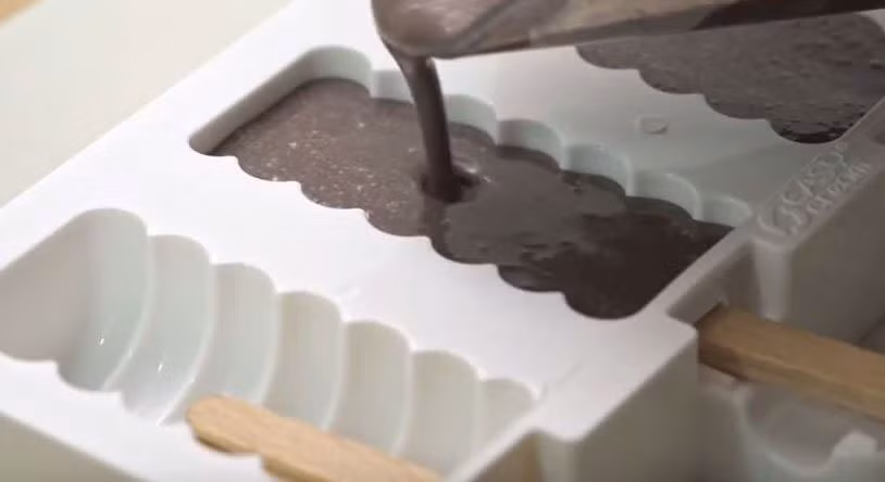 2. Kem sữa nhúng. Nguyên liệu cho món kem này chỉ cần sữa, kem tươi, đường, vani, chocolate, lạc. Đun sôi nhẹ sữa, kem tươi, đường, vani rồi để nguội và đổ hỗn hợp vào khuôn để làm thành kem. Đun chảy chocolate, đổ ra giấy thấm dầu rồi cắt thành những hình tròn to - nhỏ. Lấy kem ra khỏi khuôn. Ảnh: idp.vn.