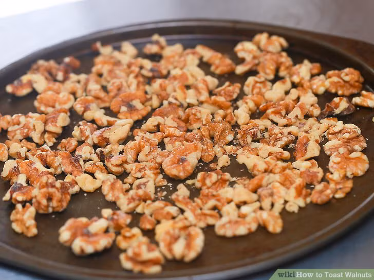 3. Kẹo caramel quả óc chó. Nguyên liệu: Kem tươi, đường nâu, bơ nhạt, siro vị ngô, siro phong, tinh chất vani, bột quế, bột nhục đậu khấu, bột đinh hương đất, ớt cayene, muối, quả óc chó. Rải đều tấm giấy nến để chống dính cho khay chữ nhật. Hãy rắc đều quả óc chó lên trên khay nướng. Đem vào lò nướng chừng 10 phút hoặc lâu hơn để hạt trở nên màu nâu đều. Ảnh: wikihow.com.