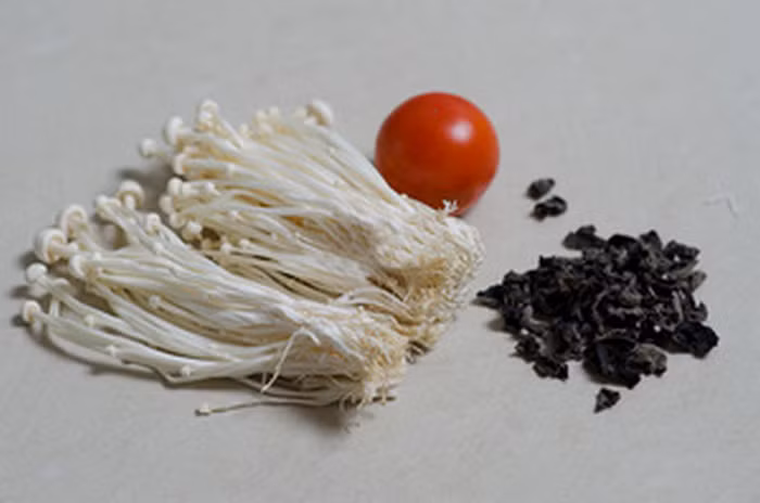 Salad nấm kim châm. Chuẩn bị mộc nhĩ, nấm kim châm, cà chua, muối, dầu, giấm, nêm. Nấm kim châm rửa sạch với nước muối, mộc nhĩ ngâm nước ấm rồi rửa sạch, cà chua rửa sạch bỏ hạt thái sợi. Thả mục nhĩ vào nước sôi đun 3 phút rồi vớt ra để ráo thái sợi. Chần sơ nấm kim châm với nước ấm rồi vớt ra để ráo nước. Ảnh: Bepnha.