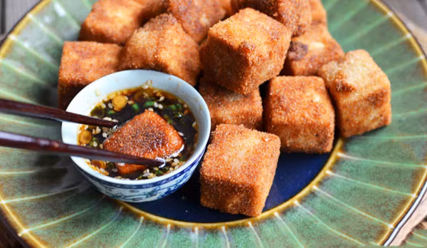 Trộn bột bắp và bột ngũ vị hương vào 1 cái đĩa. Sau đó, nhúng đậu hũ non vào hỗn hợp bột bắp, đến trứng gà rồi qua 1 lớp bột chiên xù. Làm nóng dầu ăn trong chảo, cho đậu hũ non vào, chiên giòn. Thỉnh thoảng lật đều để đậu hũ không bị cháy. Ăn đậu với cơm và chấm kèm nước tương hoặc tương ớt sẽ ngon hơn. Ảnh: aFamily.vn.