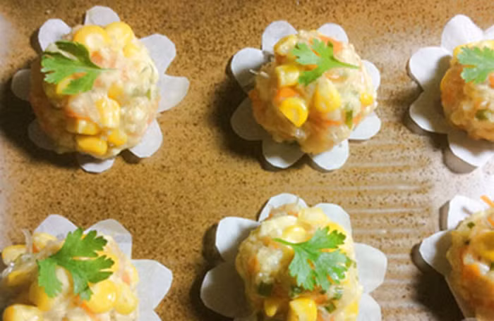 Trộn nửa ngô cùng các nguyên liệu đã thái trên, cho thêm 1 thìa nhỏ hạt nêm trộn đều. Sau đó viên tròn hỗn hợp và ấn thêm một số hạt ngô xung quanh. Cho giấy thấm dầu lót dưới giá hấp rồi đặt các viên ngô lên và đem đi hấp. Ảnh: Amthucchay.