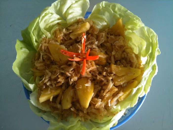 4. Tép khô xào dứa. Nguyên liệu gồm tép khô, dứa chín, gia vị hạt tiêu, mắm muối, xà lách, ớt. Tép khô ngâm vào nước lạnh, dùng tay khuấy cho cát lắng xuống, đổ nước bẩn đi rồi lặp lại vài lần cho sạch tép khô. Đổ tép vào một cái rổ để ráo nước. Dứa rửa sạch, cắt bỏ phần cuốn ở giữa rồi cắt thành miếng nhỏ vừa ăn. Ảnh: Chodokho.