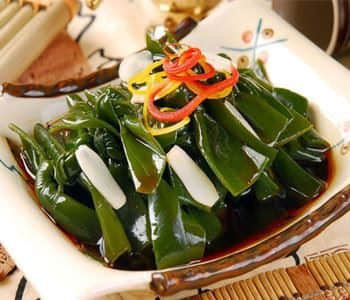 Băm nhỏ tỏi, thêm vào đó một chút nước tương, giấm, đường và muối, sau đó khuấy đều ta được hỗn hợp nước sốt. Trộn đều tảo bẹ, cà rốt và dưa chuột trong một chiếc xoong, sau đó thêm nước sôi vào chần qua và vớt ra để ráo nước. Sau khi trộn đều tảo bẹ, cà rốt và dưa chuột, ta sẽ thêm một chút dầu mè và hỗn hợp nước sốt, khuấy đều. Ảnh: zuocai.tv.