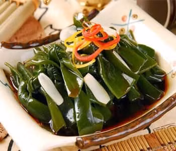 Băm nhỏ tỏi, thêm vào đó một chút nước tương, giấm, đường và muối, sau đó khuấy đều ta được hỗn hợp nước sốt. Trộn đều tảo bẹ, cà rốt và dưa chuột trong một chiếc xoong, sau đó thêm nước sôi vào chần qua và vớt ra để ráo nước. Sau khi trộn đều tảo bẹ, cà rốt và dưa chuột, ta sẽ thêm một chút dầu mè và hỗn hợp nước sốt, khuấy đều. Ảnh: zuocai.tv.