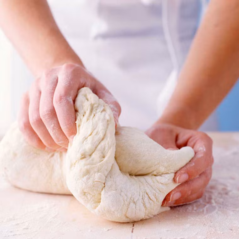 Mở nắp và thử ấn vào hỗn hợp. Nếu bột nở chính xác, nó sẽ thụt vào rồi từ từ xẹp xuống. Dùng tay hoặc thìa cao su để gấp bột từ mép vào giữa bát. Xoay bát 90 độ và lặp lại động tác đến khi tất cả bột ở hai bên được gấp vào giữa. Sau khi hoàn tất, đậy lại để hỗn hợp tiếp tục nở thêm khoảng 1 tiếng rưỡi đến 2 tiếng. Ảnh: bachhoaxanh.vn.