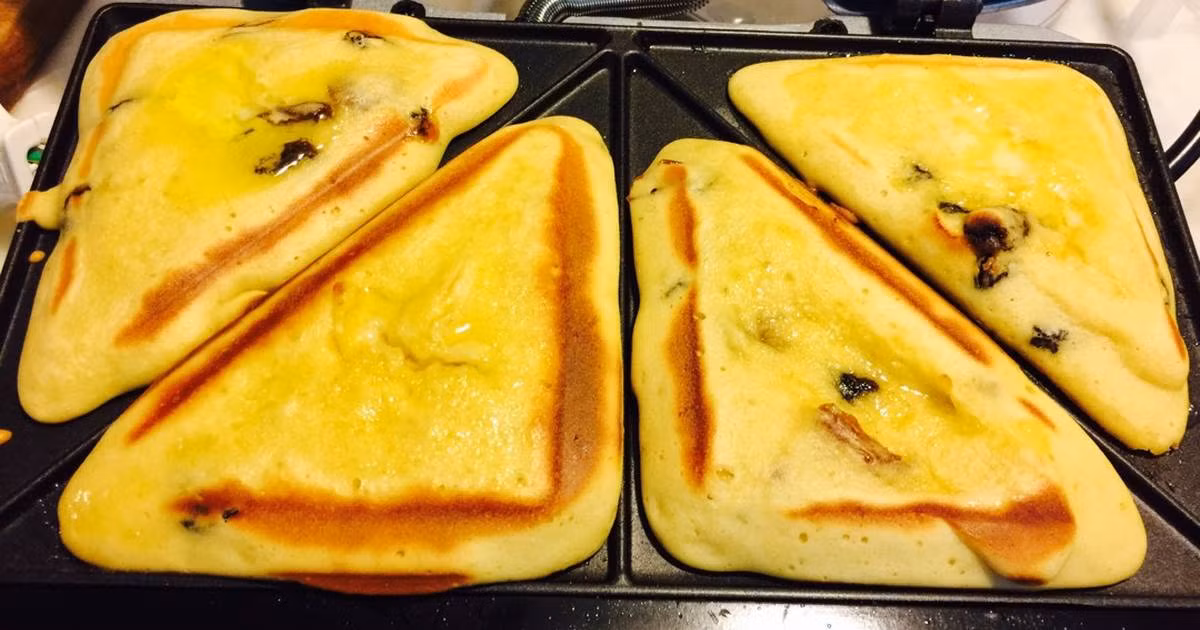 Trộn trái chà là khô, nho khô vào bột đã đánh bông. Nồi hotdog cắm điện và phết lớp bơ rồi dùng thìa canh múc một thìa canh đậy bột cho vào từng khay. Khi xong 4 ô thì đậy lại và khi nó chuyển đèn xanh thì mở nắp, bánh chín. Ảnh: cookpad.com.