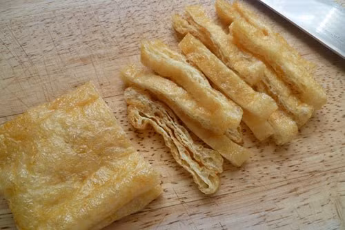 Cắt lát miếng đậu hũ chiên. Sau đó cho vào chảo dầu nóng chiên lại rồi cắt sợi. Tàu hũ ky cho vào chảo dầu chiên giòn. Cần tây cắt sợi, hành rửa sạch băm nhỏ. Cà rốt các bạn đem gọt vỏ và rửa sạch sau đó bào sợi. Pha nước tương theo công thức 1,5 thìa bột ngọt+ 1 thìa nước tương+ 1/2 thìa muối+ ½ thìa đường khuấy đều. Ảnh: Lamsao.com.