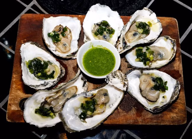 1. Hàu sống chấm với mù tạt: Nguyên liệu: Hàu, mù tạt, tỏi, ớt, nước tương, chanh, rau răm, ngò. Thịt hàu được lấy ra khi tách khỏi phần vỏ, rửa sạch để tủ lạnh 30 phút. Vắt chanh vào lớp trên của hàu, lấy thịt hàu ra và chấm với mù tạt và thưởng thức. Ảnh: Hotdeal.vn.