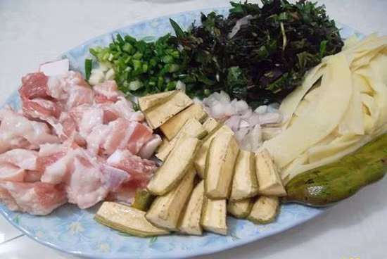 Chuối xanh gọt tước vỏ, bổ làm đôi, cắt khúc 3cm ngâm trong nước pha muối khoảng 15 phút vớt ra, cho vào xoong nước luộc chín tới. Cà chua rửa sạch, thái lát mỏng, bỏ hạt. Đậu thái miếng như chuối. Nghệ rửa sạch cạo vỏ giã nát lấy nước cốt. Hành, tỏi bóc vỏ băm nhỏ. Ảnh: toinayangi.vn.