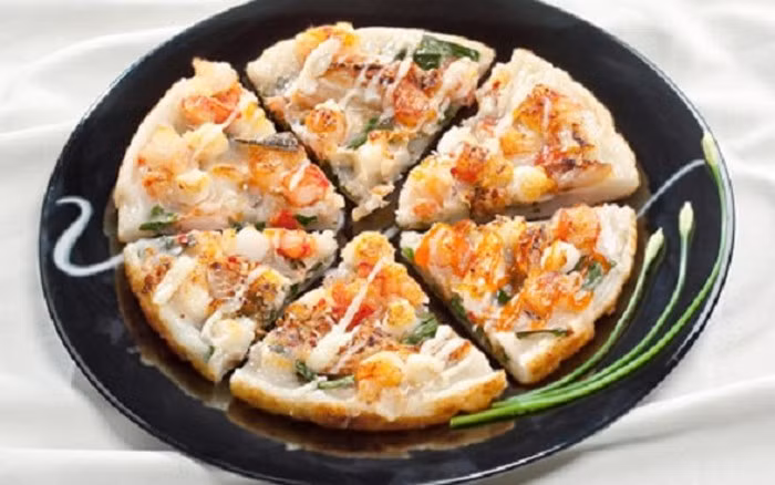 Bắc chảo lên bếp, cho dầu vào. Khi dầu sôi thì cho 1 muỗng bột vào, dàn đều. Sau đó, bạn trải các loại hải sản lên trên cùng với ớt tươi. Đổ 1/3 lượng trứng lên trên phần nhân hải sản. Chiên bánh với mức lửa vừa từ 2 – 3 phút rồi dùng muôi dẹt lật mặt bánh, chiên tiếp khoảng 2-3 phút nữa. Khi bánh chín đều 2 mặt là hoàn thành món bánh. Ảnh: Cachlam9.