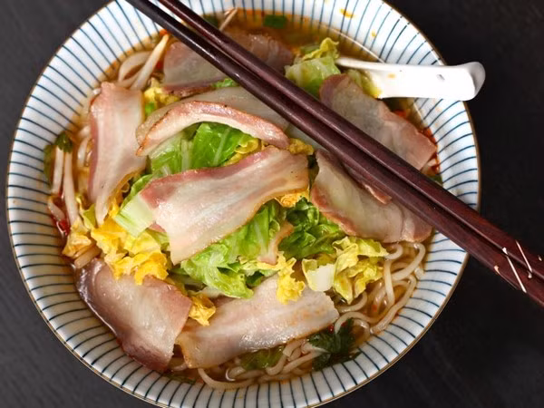  Cho thêm một vài lát thịt hun khói: Cho 2 lát thịt hun khói cắt thành từng miếng vừa ăn và một vài lá bắp cải thái nhỏ vào nồi khoảng 2 phút trước khi mỳ chín. Ảnh: HaVietfoods.vn.