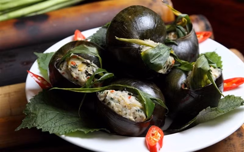 Vỏ ốc rửa sạch, trụng qua nước sôi, để ráo. Băm nhỏ thịt ốc trộn với giò sống, thịt nạc xay, nấm mèo thái nhỏ và các gia vị cho vừa ăn. Cuốn hỗn hợp thịt ốc vào trong lá sả, cho vào từng vỏ ốc và đem hấp chín. Dọn ốc ra đĩa, ăn kèm với tía tô, rau răm và chén nước mắm gừng. Ảnh: Cooky.vn.