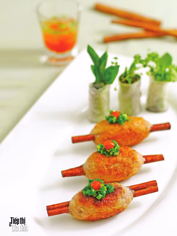 Lấy hỗn hợp thịt đã quết bọc vào quế cây. Đem thịt nướng trên bếp than chín vàng. Hành lá thái nhỏ. Phi thơm hành với mỡ. Bánh tráng cuốn với rau sống. Xếp các chạo ra đĩa, dùng kèm với mỡ hành và các cuộn rau sống. Ảnh: tiepthigiadinh.sunflower.vn.