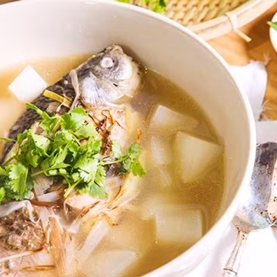 Cho cá chép và củ cà rốt vào trước. Khi nước canh sôi lần 2 thì cho củ cải trắng vào. Vớt bỏ bọt canh để nước canh trong. Nêm gia vị, cho hành lá, ớt băm và ngò rí vào. Tắt bếp, rắc tiêu lên trên. Ảnh: Cooky.vn.