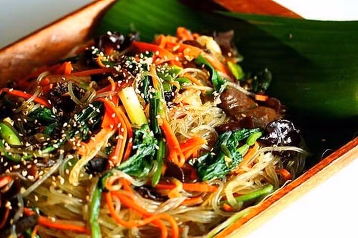 Cà rốt, hành tây, nấm thái sợi, hành lá thái nhỏ, băm tỏi nhỏ. Rau cải xoăn chần qua nước sôi. Thịt bò cũng cắt sợi như cọng tăm rồi ướp gia vị và xào sơ qua. Cho dầu vào chảo phi thơm tỏi và cho rau củ và nấm vào xào. Nêm vừa miệng thì cho miến và rau cải xoăn vào xào, cuối cùng là cho thịt bò vào trộn đều. Rắc hành lá, mè lên cho thơm là đã được món xào kiểu Hàn ngon tuyệt. Ảnh: Laodong.