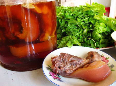 Thịt chân giò cuộn lại, lấy dây buộc vòng quanh miếng thịt chặt 1 chút. Luộc sơ qua thịt rồi đổ nước đi. Lấy nước mới rồi cho hành khô đập dập, bột nêm, gia vị luộc 25-30 phút sau đó gắp ra thả thịt chân giò vào tô nước lọc để thịt nguội. Ảnh:imonanngon.info.