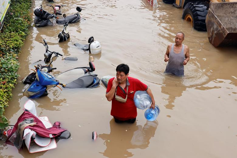 Người đàn ông mang theo bình nước lội qua con đường ngập hôm 23/7.