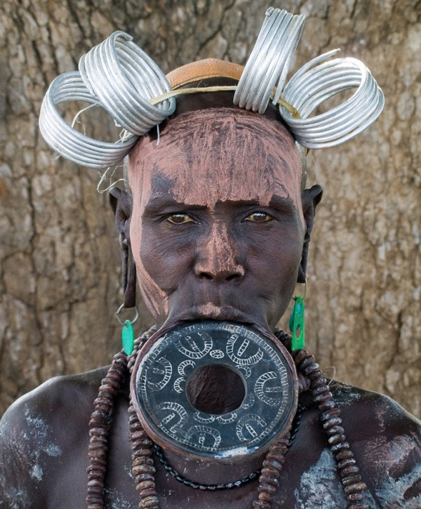 Đầu tiên, người ta làm gãy 2 chiếc răng dưới. Họ làm điều đó bằng cách dùng đá. Kế đến, người lớn tuổi trong bộ tộc đục một lỗ trên môi dưới của bé gái để đưa một nút gỗ nhỏ vào.