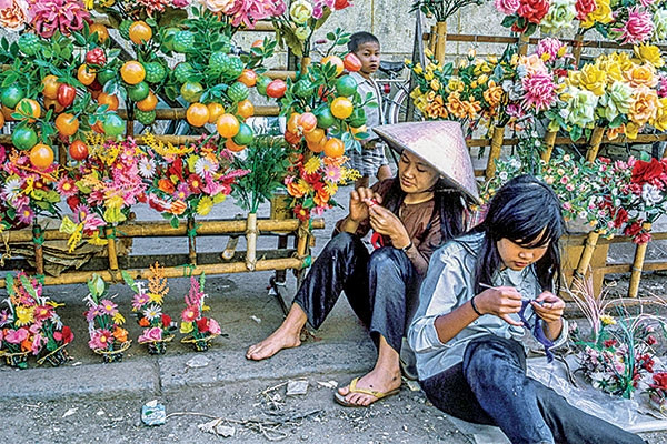 Hai cô gái vừa bán hoa giả vừa tranh thủ đan len.