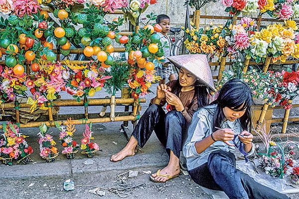 Hai cô gái vừa bán hoa giả vừa tranh thủ đan len.