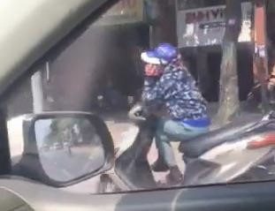 Nguoi phu nu ngoi vat cheo chan, nghe dien thoai khi dang di xe may