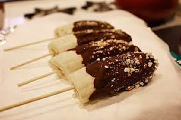 Chuối phủ socola. Món ăn làm cực nhanh mà lại rất ngon. Xiên que kem lần lượt vào các nửa quả chuối. Xếp các nửa quả chuối này vào khay và để trên ngăn đá 2 giờ hoặc qua đêm. Đun socola tan chảy sau đó nhúng chuối phủ nửa socola. Muốn đẹp mắt và lạ miệng hơn thì bạn hãy rắc các loại hạt cốm, hạnh nhân vỡ tùy thích.