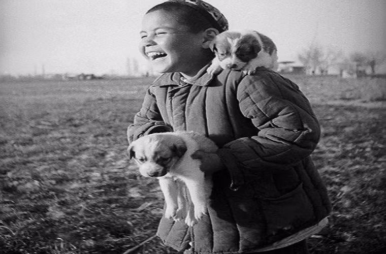 Bé trai cười tươi khi bế hai chú cún cưng trong một nông trại tập thể ở đất nước Uzbekistan nhiều năm về trước.