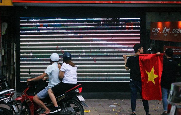 Hình ảnh màn hình lớn được một cửa shop giày trên đường phố Hai Bà Trưng lắp ra phía ngoài đường để cho cổ động viên theo dõi trận thi đấu giữa U23 Việt Nam - U23 UAE.