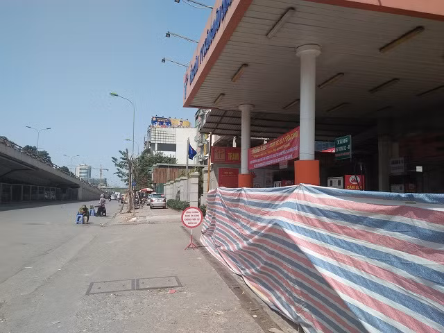 Ngồi ngay trước trạm xăng bán xăng với giá đắt, trước dòng chữ lưu ý không nên mua hàng.