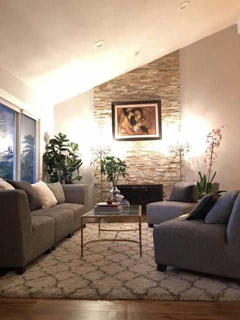 Phòng khách nhỏ nhưng ấm cúng với ghế sofa màu xám nhạt sang trọng và bàn kính hiện đại, ấm cúng với gam màu vàng của đèn. Ngoài ra phòng khách còn có khá nhiều cây xanh giúp không khí trong nhà luôn dễ chịu và trong lành.