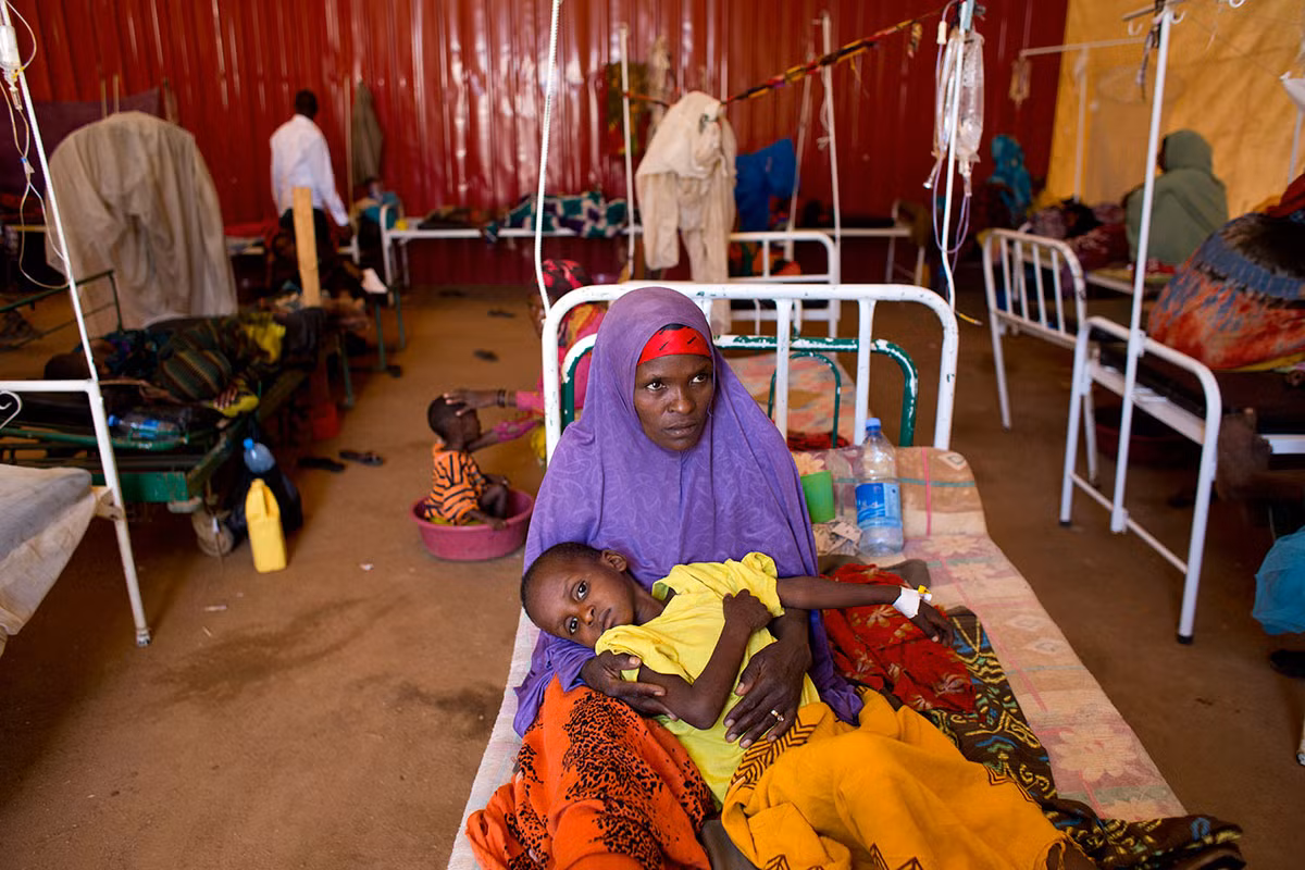 Hawa Ibrahim bế cậu con trai 10 tuổi, Andi Nassir, trên giường bệnh. Các bà mẹ cho biết, nước sạch được bán ở một số khu vực nhưng do quá đắt nên họ không có tiền mua.