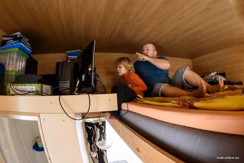 Hai bố con ngồi trên giường ngủ và xem ti vi. Ngôi nhà tuy chật chội nhưng khá ấm cúng.