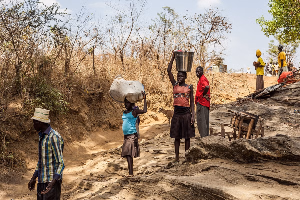 Một nhóm người tị nạn mang theo đồ đạc chờ đến lượt qua suối Kayo.