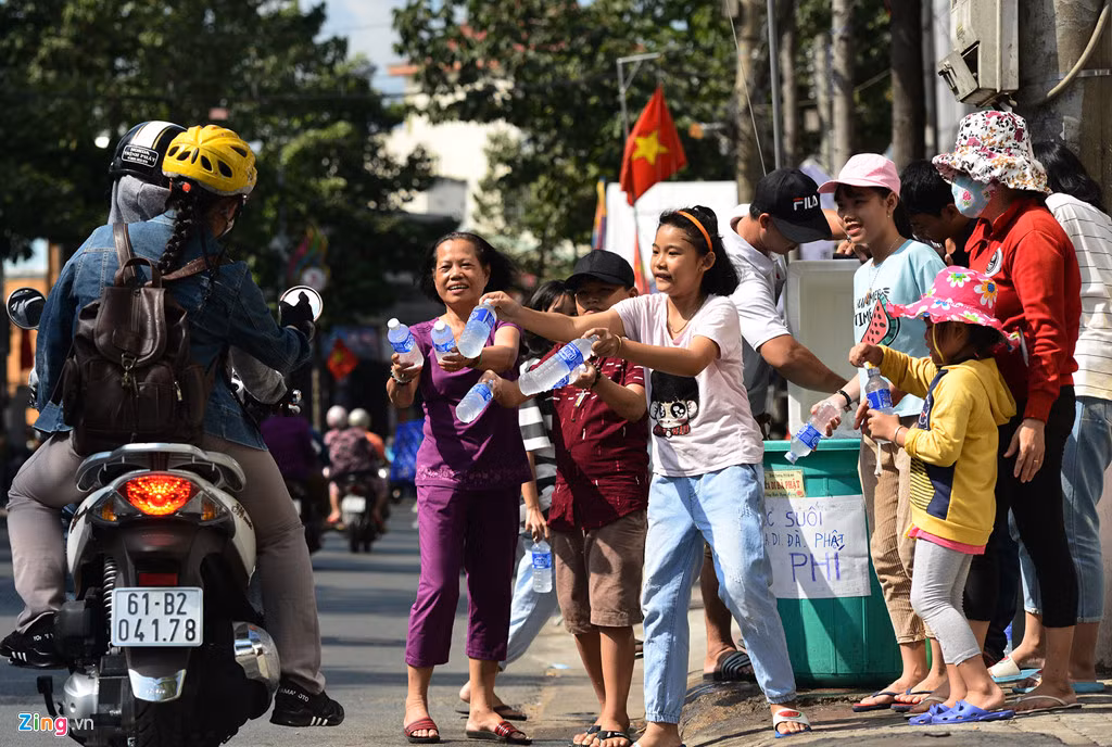 Trên đường Thích Quảng Đức, hàng chục già trẻ, con cháu gia đình anh Nguyễn Hồng Khanh (phường Hiệp Thành) đội nắng liên tục phát hơn 40 lốc nước suối ướp lạnh cho khách.