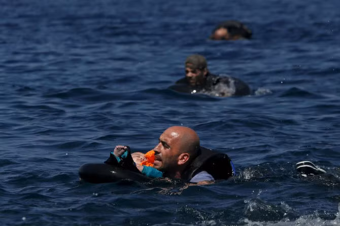 Một người tị nạn Syria vừa bế một em nhỏ vừa bơi vào bờ ở đảo Lesbos, Hy Lạp ngày 13/9.