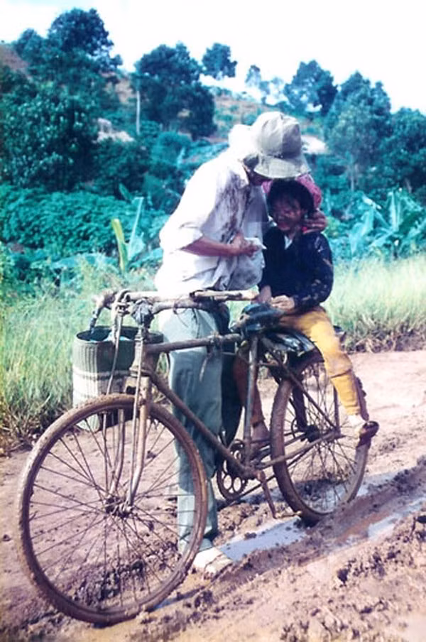Hai cha con bên chiếc xe đạp cũ vượt qua đoạn đường đầy bùn đất, người cha dừng lại lấy áo mình lau bùn ấm lem trên mặt con gái.