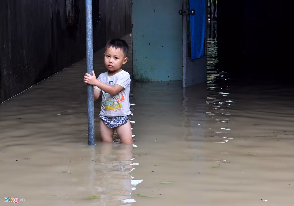 Bé Nguyễn Chí Cường (8 tuổi, ngụ xã Phú Cường) đứng bơ vơ trước hiên nhà khi nước lũ ngập mọi nơi.