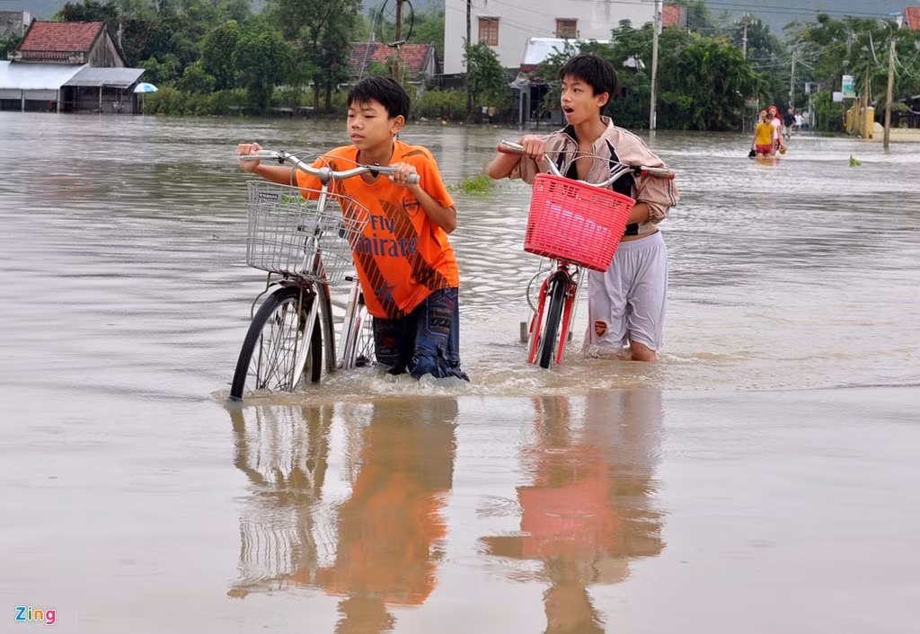 Trẻ em dắt xe bì bõm trên đường ngập nước lũ.
