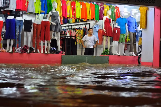 Nước dâng tại khu dân cư phường Long Bình khiến chủ cửa hành kinh doanh quần áo phải kê đồ lên cao rồi dùng tấm thép chắn cửa để ngăn ngập vào trong.