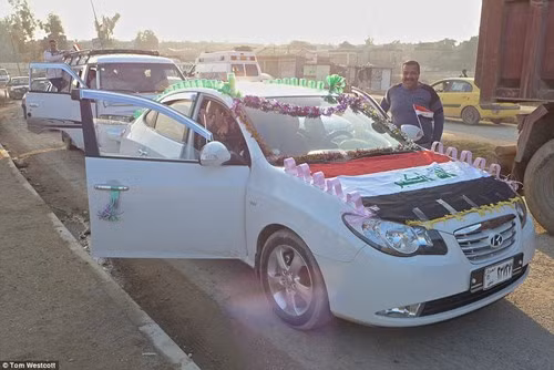 Đây là đám cưới công khai đầu tiên được tổ chức kể từ sau khi một phần của Mosul được giải phóng khỏi IS. Trong ảnh: chiếc xe cưới được trang trí đơn giản cùng quốc kì Iraq.