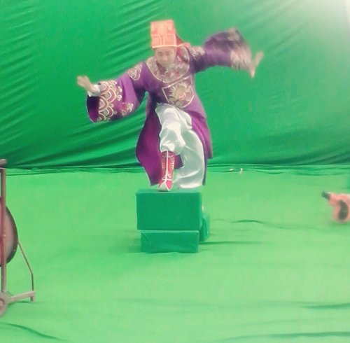 Nghệ sĩ Tự Long đang tạo dáng Táo cưỡi trên mây để đi lên thiên đình. Tấm phông xanh phía sau cho thấy, những cảnh quay này sẽ được dùng kỹ xảo máy tính để mang đến cho khán giả những hình ảnh hấp dẫn.