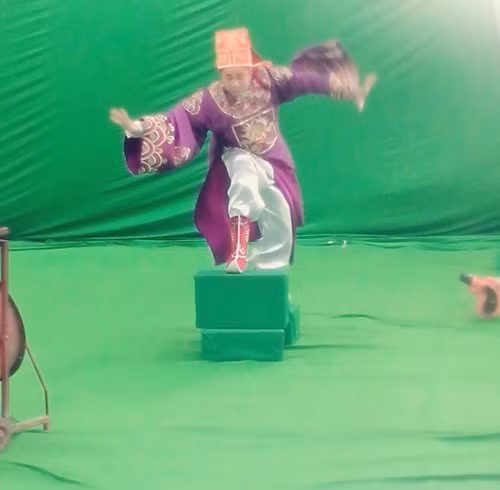 Nghệ sĩ Tự Long đang tạo dáng Táo cưỡi trên mây để đi lên thiên đình. Tấm phông xanh phía sau cho thấy, những cảnh quay này sẽ được dùng kỹ xảo máy tính để mang đến cho khán giả những hình ảnh hấp dẫn.