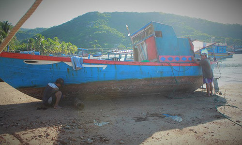 Sáu Thanh và Hai Mạnh tranh thủ cạo xác hà bên mạn thuyền râm mát khi mặt trời dần lên cao. Ảnh: Hoàng Như.